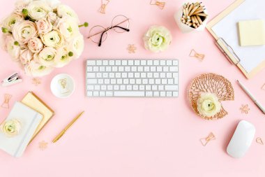 Tarz sahibi, pembe kadınların ofis masası. Bilgisayarlı çalışma alanı, buket ranunculus ve güller, pembe arka planda pano. Düz yatıyordu. Üst görünüm.