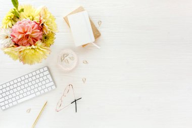 Düz uzanmış kadınların ofis masası. Sarı yıldız çiçekleri, aksesuarlar, altın günlük, beyaz ahşap arka plan. Üst görünüm.