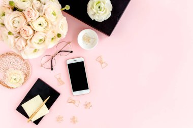 Tarz sahibi, pembe kadınların ofis masası. Bilgisayarlı çalışma alanı, buket ranunculus ve güller, pembe arka planda telefon. Düz yatıyordu. Üst görünüm.