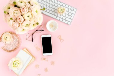 Tarz sahibi, pembe kadınların ofis masası. Bilgisayarlı çalışma alanı, buket ranunculus ve güller, pembe arka planda telefon. Düz yatıyordu. Üst görünüm.