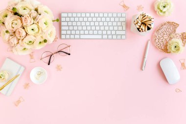 Tarz sahibi, pembe kadınların ofis masası. Bilgisayarlı çalışma alanı, buket ranunculus ve güller, pembe arka planda pano. Düz yatıyordu. Üst görünüm.