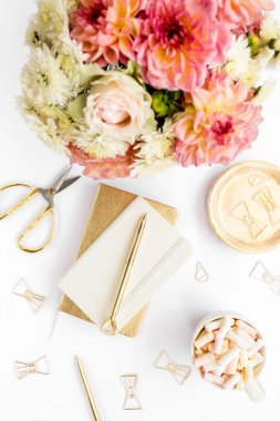 Ev ofisinin masası düzdü. Pembe güllü kadın çalışma alanı, yıldız çiçeği buketi, altın aksesuarlar, beyaz arka planda günlük. Üst görünüm.