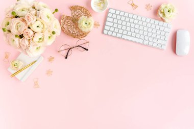 Tarz sahibi, pembe kadınların ofis masası. Bilgisayarlı çalışma alanı, buket ranunculus ve güller, pembe arka planda pano. Düz yatıyordu. Üst görünüm.