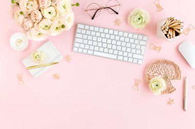 Tarz sahibi, pembe kadınların ofis masası. Bilgisayarlı çalışma alanı, buket ranunculus ve güller, pembe arka planda pano. Düz yatıyordu. Üst görünüm.