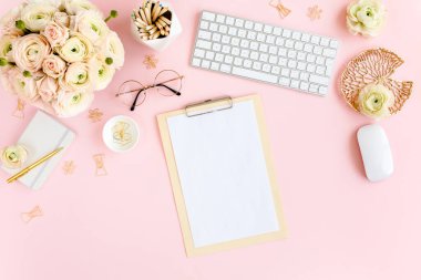 Tarz sahibi, pembe kadınların ofis masası. Bilgisayarlı çalışma alanı, buket ranunculus ve güller, pembe arka planda pano. Düz yatıyordu. Üst görünüm.