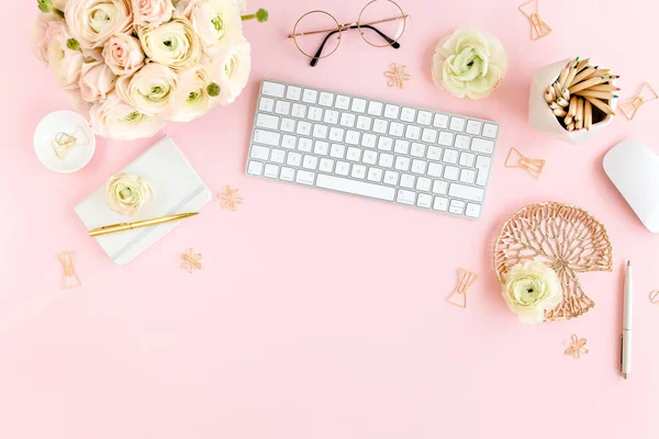 Stylized, pink womens home office desk. Workspace with computer, bouquet ranunculus and roses, clipboard on pink background. Flat lay. Top view.