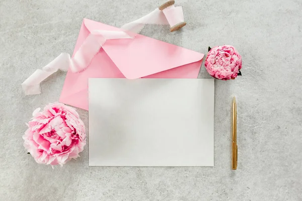 초대, 빈 종이 인사말 카드 회색 테이블 위의 핑크 봉투와 고추. 꽃 배경. 평평하게 누워 있는 위에서 바라본 모습. — 스톡 사진