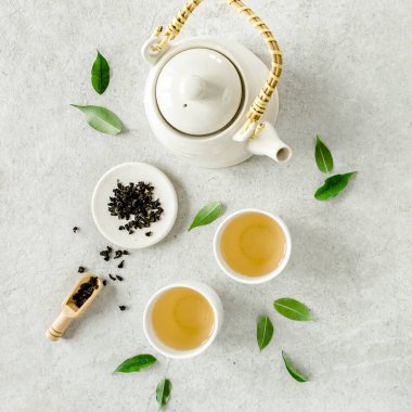 İki beyaz çay fincanı ve yeşil çay yapraklı çaydanlık ile bitki çayı. Düz yerde, üst tarafta. Çay konsepti