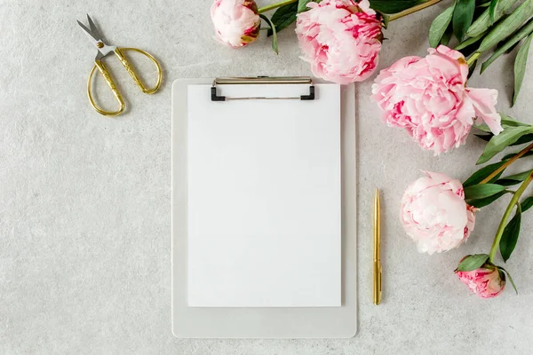 Sahte davetiye, boş kağıt tebrik kartı ve gri taş masadaki şakayıklar. Çiçek arkaplanı. Düz yatış, üst görünüm.