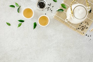 İki beyaz çay fincanı ve yeşil çay yapraklı çaydanlık ile bitki çayı. Düz yerde, üst tarafta. Çay konsepti