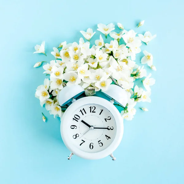 Composition-Heure d'été de Jasmin fleur et horloge, alarme sur fond bleu. Couché plat, vue du dessus — Photo