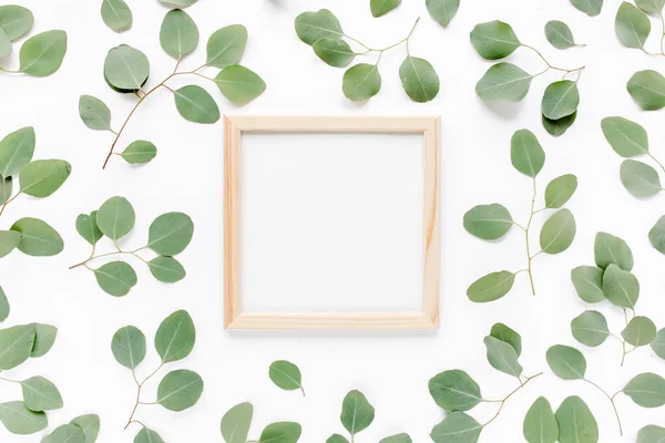 Square frame decorated with green eucalyptus leaves, twigs, floral pattern on a white background. The apartment lay, top view. Floral frame.