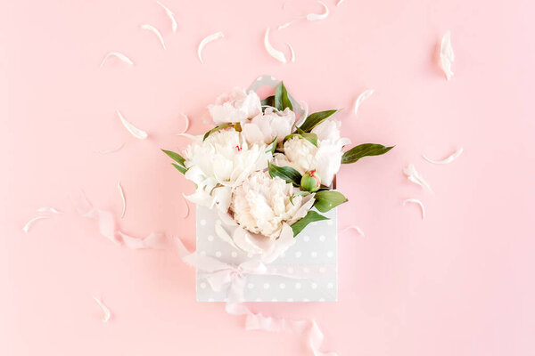Beige bouquet of peonies in an envelope for flowers on pink background. Minimal floral concept greeting card. Flat lay, top view. 