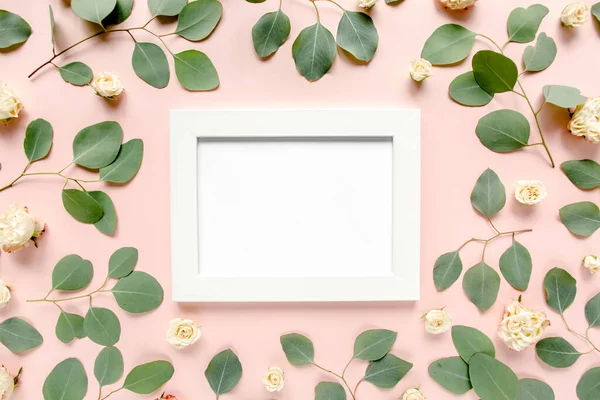 Біла рамка прикрашена зеленим листям евкаліпта, трояндами, квітковим візерунком на рожевому тлі. Квартира лежала, вид зверху. Квіткова рамка . — стокове фото