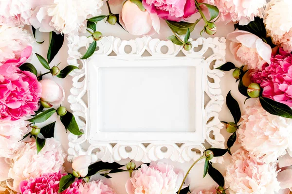 Carved, white frame decorated of beautiful pink peonies on white background. Flat lay, top view. Valentines background. Floral frame. Peony texture.