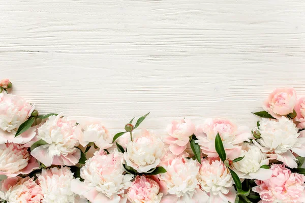 Ghirlanda a cornice floreale composta da boccioli di fiori di peonie rosa e beige, rami di eucalipto e foglie isolate su fondo bianco in legno. Posa piatta, vista dall'alto — Foto Stock