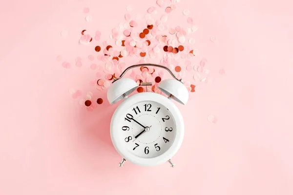 Reloj despertador blanco con vista superior cubierto de confeti dorado sobre fondo rosa. Plantilla de blog femenino de redes sociales. Estilo mínimo. plano laico — Foto de Stock