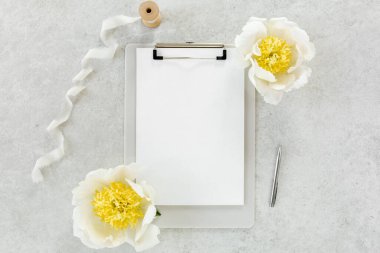 Sahte davetiye, boş kağıt tebrik kartı ve gri taş masadaki şakayıklar. Çiçek arkaplanı. Düz yatış, üst görünüm.