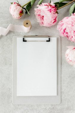 Sahte davetiye, boş kağıt tebrik kartı ve gri taş masadaki şakayıklar. Çiçek arkaplanı. Düz yatış, üst görünüm.