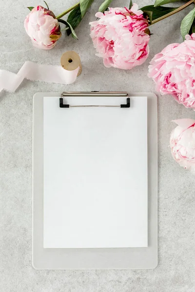 Sahte davetiye, boş kağıt tebrik kartı ve gri taş masadaki şakayıklar. Çiçek arkaplanı. Düz yatış, üst görünüm.