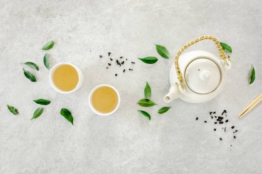 İki beyaz çay fincanı ve yeşil çay yapraklı çaydanlık ile bitki çayı. Düz yerde, üst tarafta. Çay konsepti