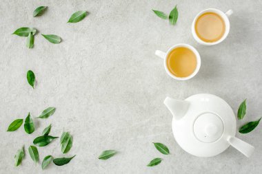 İki beyaz çay fincanı ve yeşil çay yapraklı çaydanlık ile bitki çayı. Düz yerde, üst tarafta. Çay konsepti