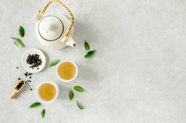 İki beyaz çay fincanı ve yeşil çay yapraklı çaydanlık ile bitki çayı. Düz yerde, üst tarafta. Çay konsepti