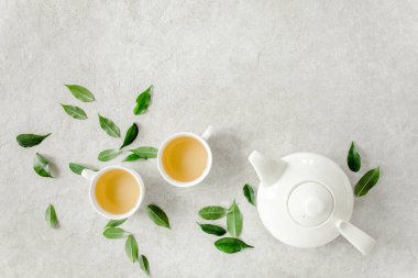 İki beyaz çay fincanı ve yeşil çay yapraklı çaydanlık ile bitki çayı. Düz yerde, üst tarafta. Çay konsepti