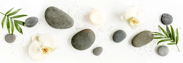 Wellness-Steine, Palmblätter, blumenweiße Orchidee, Kerze und Zen wie graue Steine auf weißem Hintergrund. Flache Lage, Draufsicht — Stockfoto