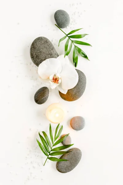 Wellness-Steine, Palmblätter, blumenweiße Orchidee, Kerze und Zen wie graue Steine auf weißem Hintergrund. Flache Lage, Draufsicht — Stockfoto