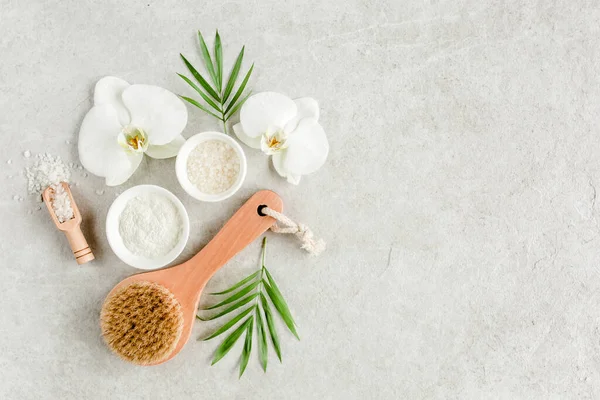 Spa behandeling concept. Natuurlijke spa cosmetica producten, zeezout, massage borstel, tropisch palmbladeren op grijze marmeren tafel van boven. Spa achtergrond — Stockfoto