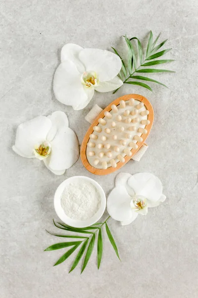 Spa treatment concept. Natural spa cosmetics products, sea salt, massage brush, tropic palm leaves on gray marble table from above. Spa background
