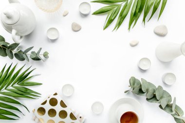 Masa çalışma alanı sulu, palmiye yaprağı dalları, çay, günlük, bardaklar ve beyaz arka planda altın tokalar. düz yatış, üst görünüm