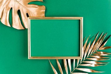 Altın tropikal palmiye yeşil arka planda Monstera ve fotoğraf çerçevesi bırakır. Düz konum, üst görünüm minimum konsept.