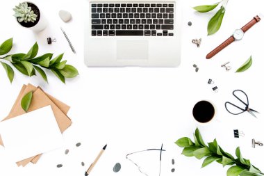 Ofis masası çalışma alanı boş, yeşil yapraklı. Dizüstü bilgisayar, beyaz arka planda gözlük. Blogcu, dergiler, sosyal medya. Düz yatış, üst görünüm.