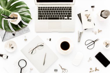 Ev ofisinin çalışma alanı dizüstü bilgisayarı, tropikal yaprakları Monstera, not panosu, defter ve aksesuarları beyaz arka planda. Düz yatış, üst görünüm