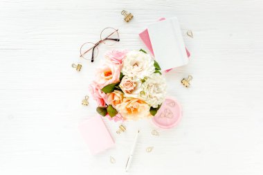 Pembe güller, çiçek buketleri, aksesuarlar, altın günlük, beyaz ahşap arka planda gözlük. Üst görünüm