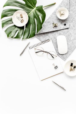 Ev ofisinin çalışma alanı dizüstü bilgisayarı, tropikal yaprakları Monstera, not panosu, defter ve aksesuarları beyaz arka planda. Düz yatış, üst görünüm