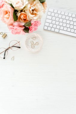 Düz uzanmış kadınların ofis masası. Bilgisayarlı kadın çalışma alanı, pembe güller çiçekler, aksesuarlar, altın günlük, beyaz arka planda gözlük. Üst görünüm 