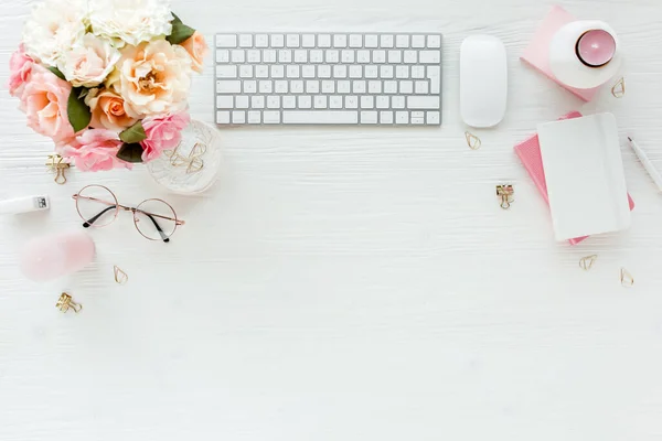 Flach lag der Schreibtisch. Weiblicher Arbeitsplatz mit Computer, rosa Rosen, Accessoires, goldenem Tagebuch, Brille auf weißem Hintergrund. Ansicht von oben — Stockfoto