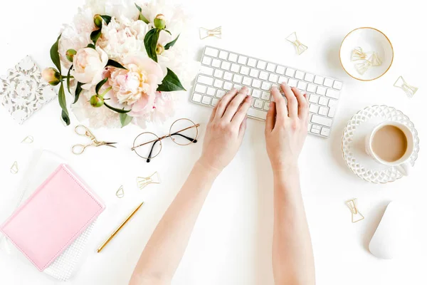 Scrivania da ufficio per donne piatte. Spazio di lavoro femminile con mani femminili, computer, bouquet di peonie rosa, accessori su sfondo bianco. Vista dall'alto. — Foto Stock