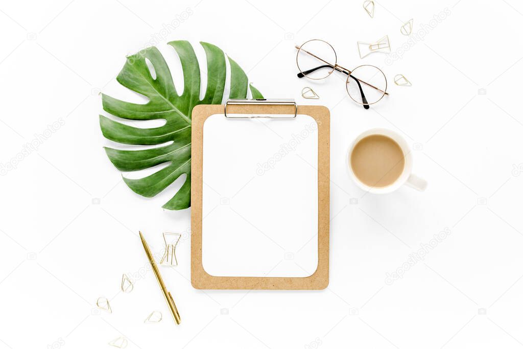 Home office workspace mockup with tropical leaves Monstera, clipboard, and accessories on white background. Flat lay, top view
