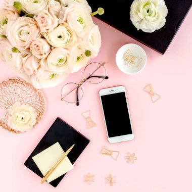 Tarz sahibi, pembe kadınların ofis masası. Bilgisayarlı çalışma alanı, buket ranunculus ve güller, pembe arka planda telefon. Düz yatıyordu. Üst görünüm.