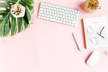 Ev ofisinin masası düzdü. Bilgisayarlı kadın çalışma alanı, tropikal palmiye yaprakları, pembe arka planda aksesuarlar. Üst görünüm arkaplanı. 