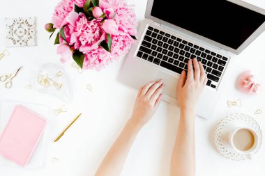 Kadın eli, dizüstü bilgisayarı, pembe şakayık buketi, beyaz arka planda aksesuarları olan bir kadın çalışma alanı. Üst görünüm kadınsı arka plan. Düz yatıyordu.