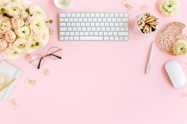 Tarz sahibi, pembe kadınların ofis masası. Bilgisayarlı çalışma alanı, buket ranunculus ve güller, pembe arka planda pano. Düz yatıyordu. Üst görünüm.