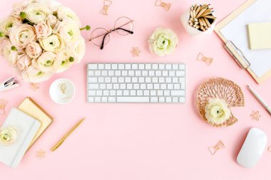 Tarz sahibi, pembe kadınların ofis masası. Bilgisayarlı çalışma alanı, buket ranunculus ve güller, pembe arka planda pano. Düz yatıyordu. Üst görünüm.