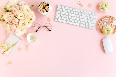 Tarz sahibi, pembe kadınların ofis masası. Bilgisayarlı çalışma alanı, buket ranunculus ve güller, pembe arka planda pano. Düz yatıyordu. Üst görünüm.