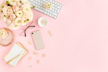 Tarz sahibi, pembe kadınların ofis masası. Bilgisayarlı çalışma alanı, buket ranunculus ve güller, pembe arka planda telefon. Düz yatıyordu. Üst görünüm.