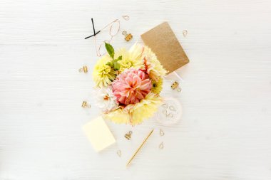 Düz uzanmış kadınların ofis masası. Sarı yıldız çiçekleri, aksesuarlar, altın günlük, beyaz ahşap arka plan. Üst görünüm.